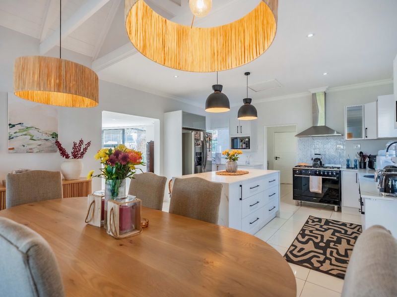 Spacious open-plan kitchen and dining area featuring a central island, modern gas range, herringbone backsplash, and vaulted ceilings with stylish pendant lighting.