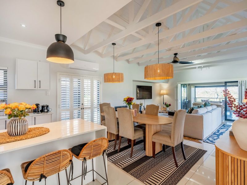 Spacious open-plan living and dining area featuring exposed white timber beams, a modern kitchen island, and seamless flow to the outdoor patio.