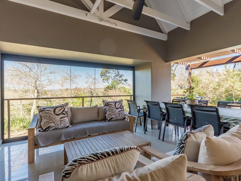 Spacious covered patio featuring a vaulted ceiling with exposed beams, tiled flooring, and glass stacker doors offering scenic outdoor views.