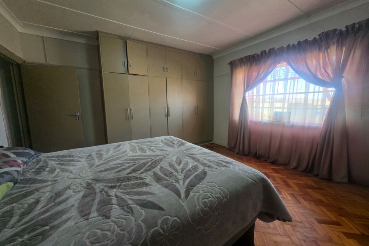 A bedroom featuring classic parquet flooring and extensive built-in cupboard storage, with security bars installed on the window.