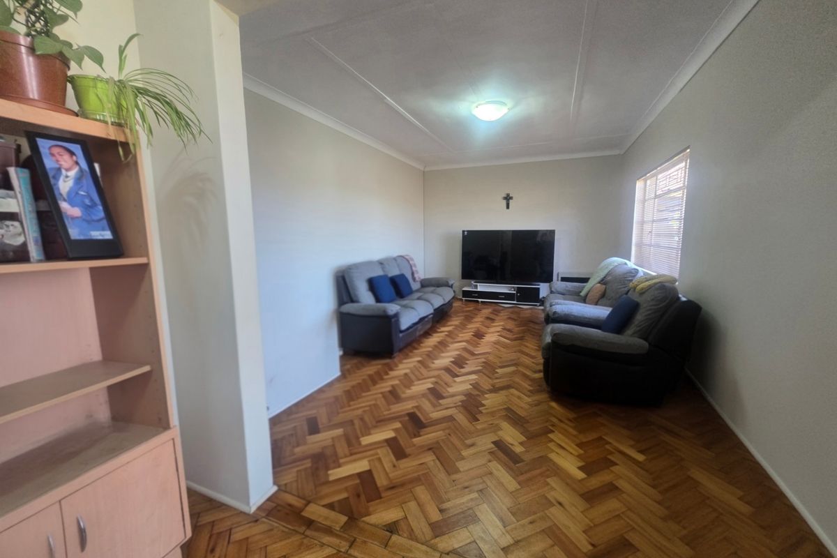 A spacious living room featuring classic herringbone parquet flooring, coved ceilings, and natural light through a side window.