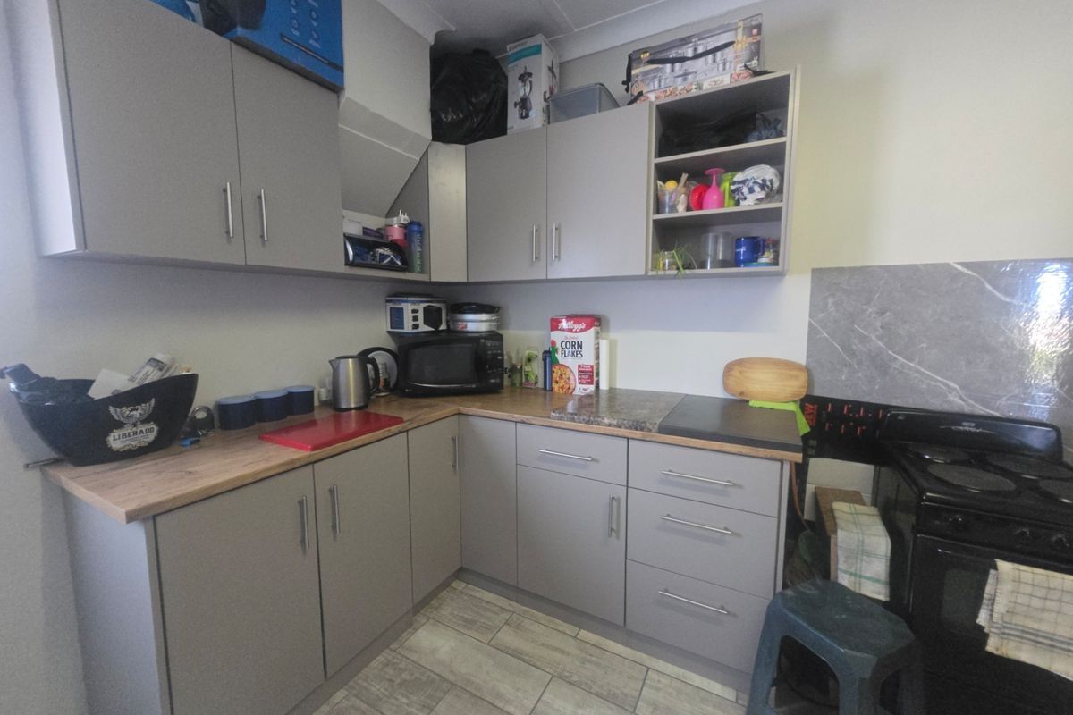 Compact kitchen featuring modern grey cabinetry, laminate countertops, tiled flooring, and a built-in electric stove with an integrated extractor fan housing.