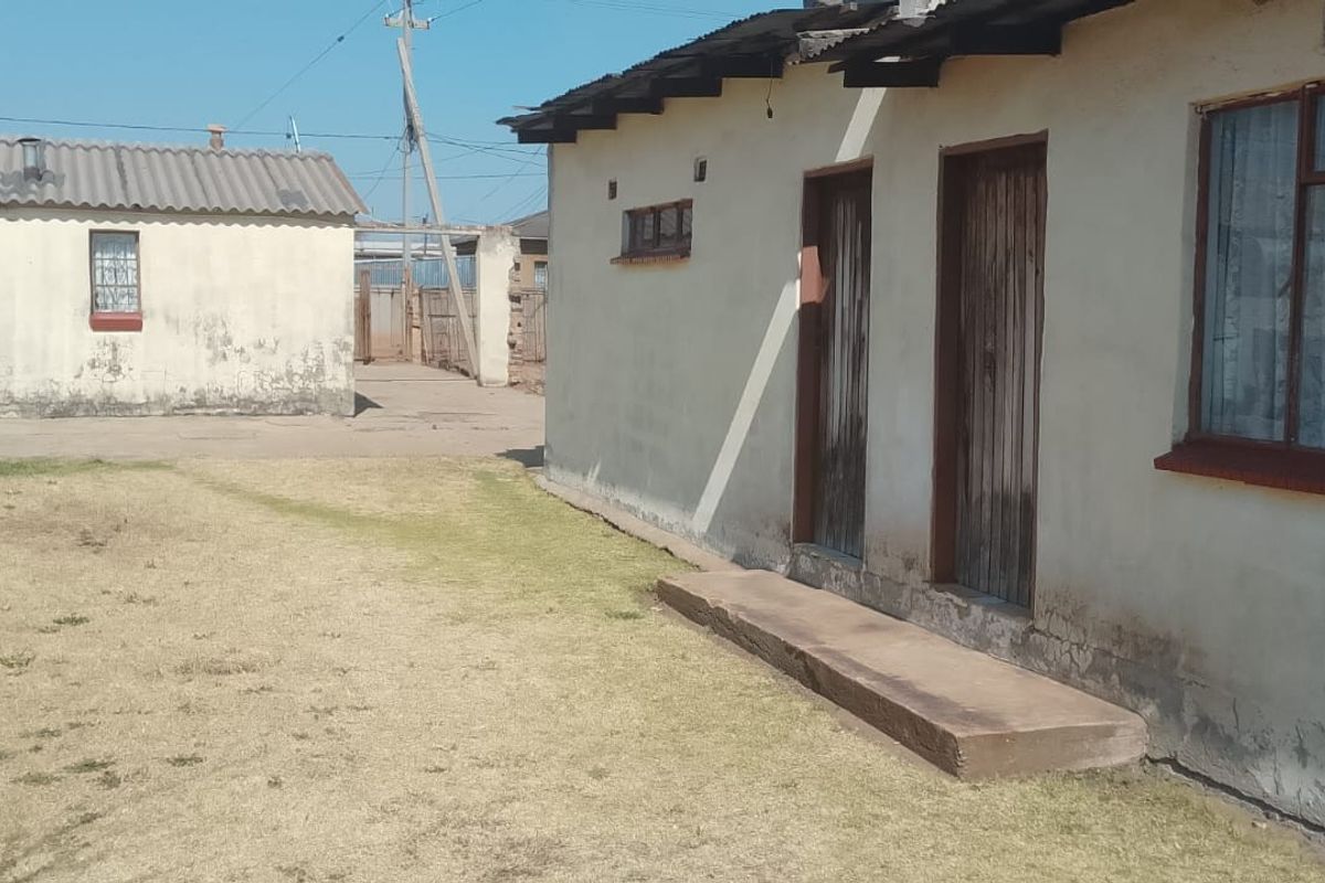 Rear view of the property showing multiple structures with weathered plaster, corrugated roofing, and basic timber door and window frames.
