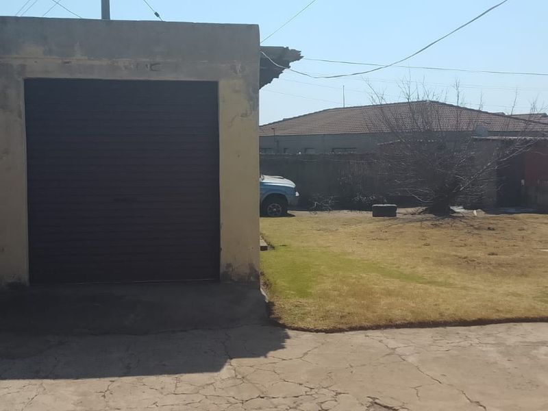Rear exterior view featuring a single garage, concrete driveway, and a grassed backyard area enclosed by boundary walls.