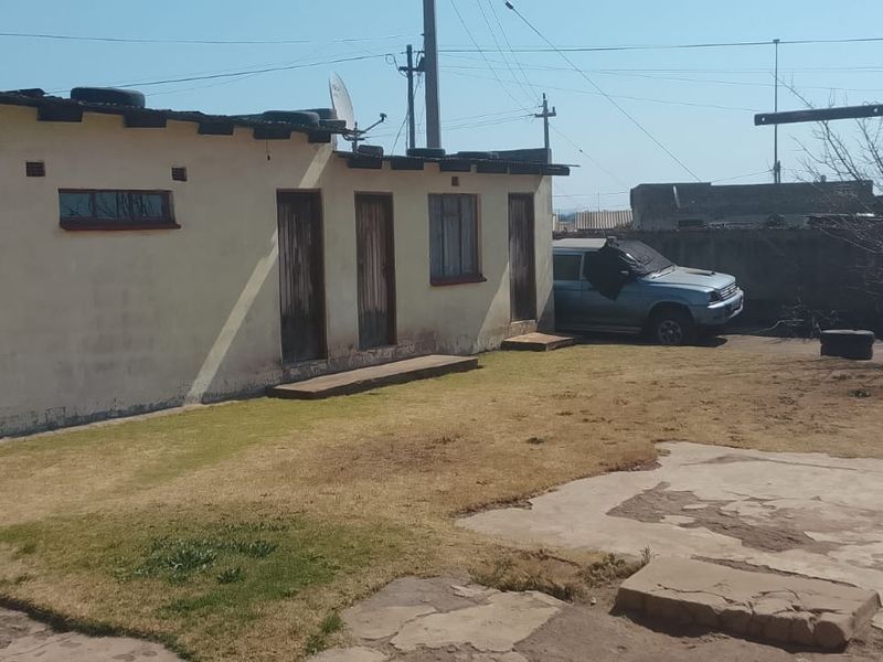 Rear exterior view of the property featuring a garage, concrete paving, and a garden area with perimeter walling.