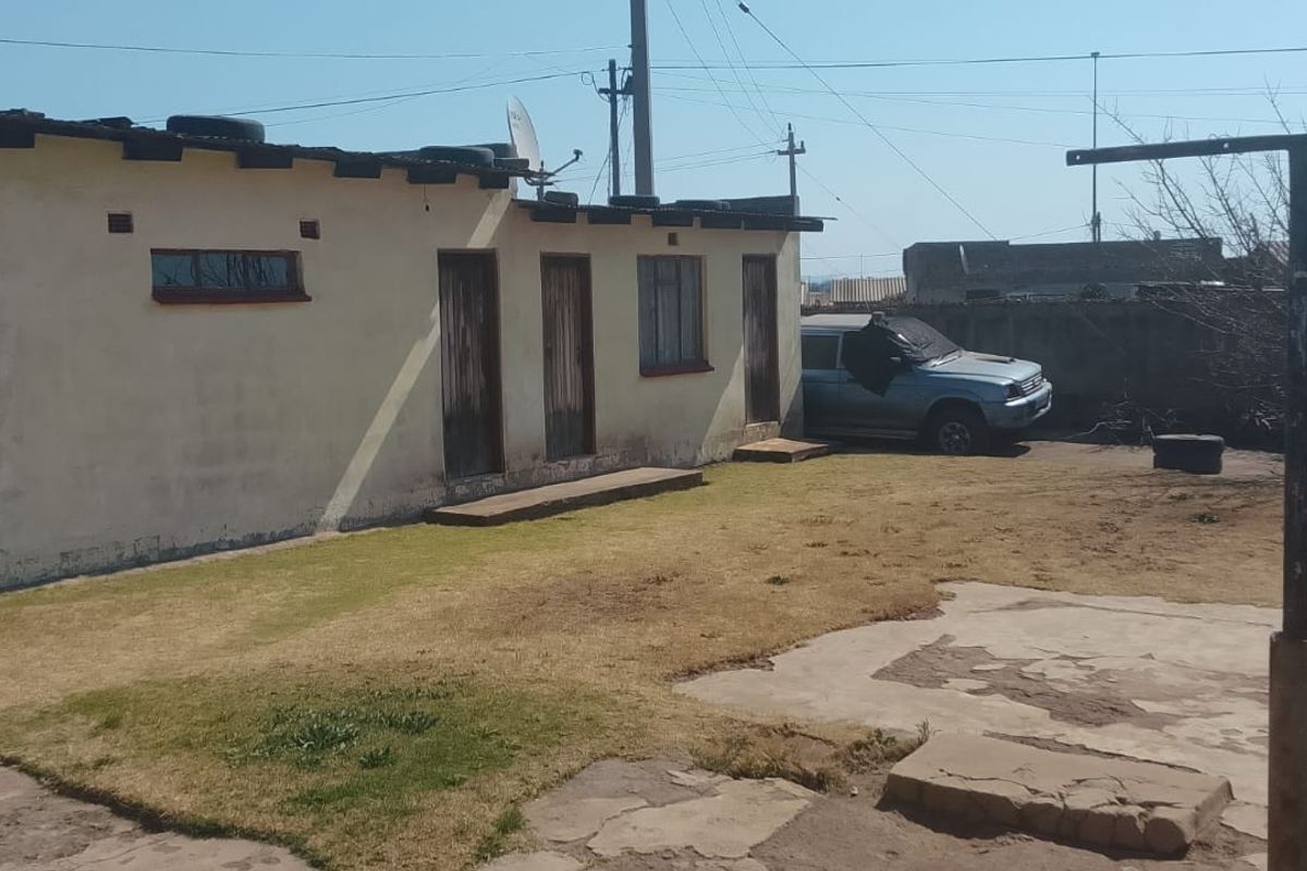 Rear exterior view of the property featuring a garage, concrete paving, and a garden area with perimeter walling.