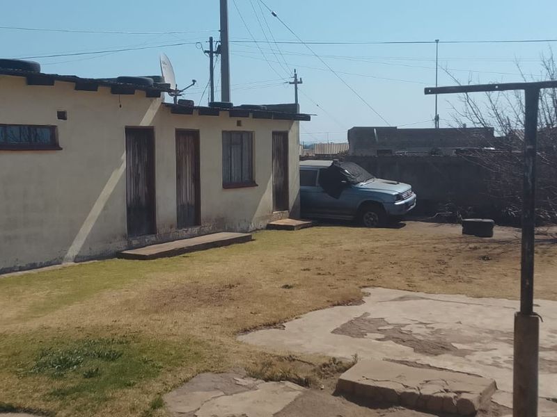 Rear exterior view of the property featuring a concrete patio area, washing line, and boundary wall with weathered exterior finishes.