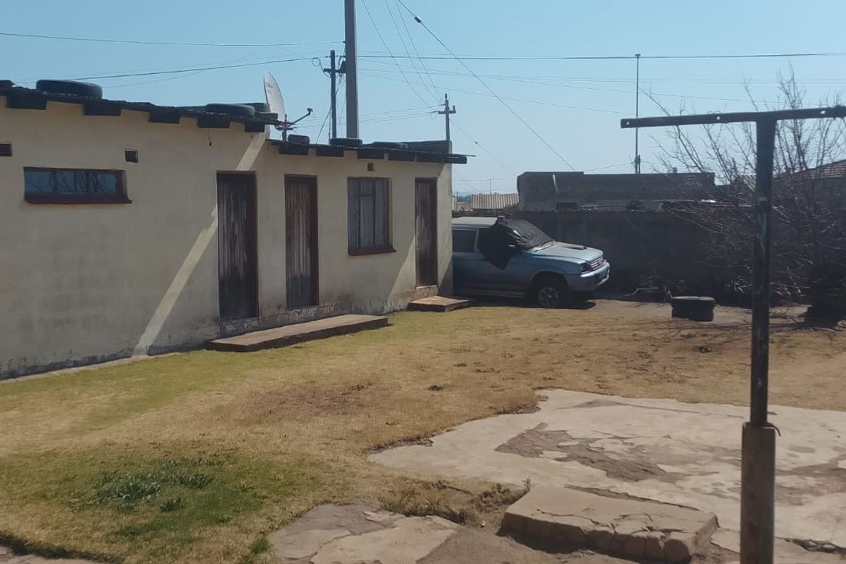Rear exterior view of the property featuring a concrete patio area, washing line, and boundary wall with weathered exterior finishes.