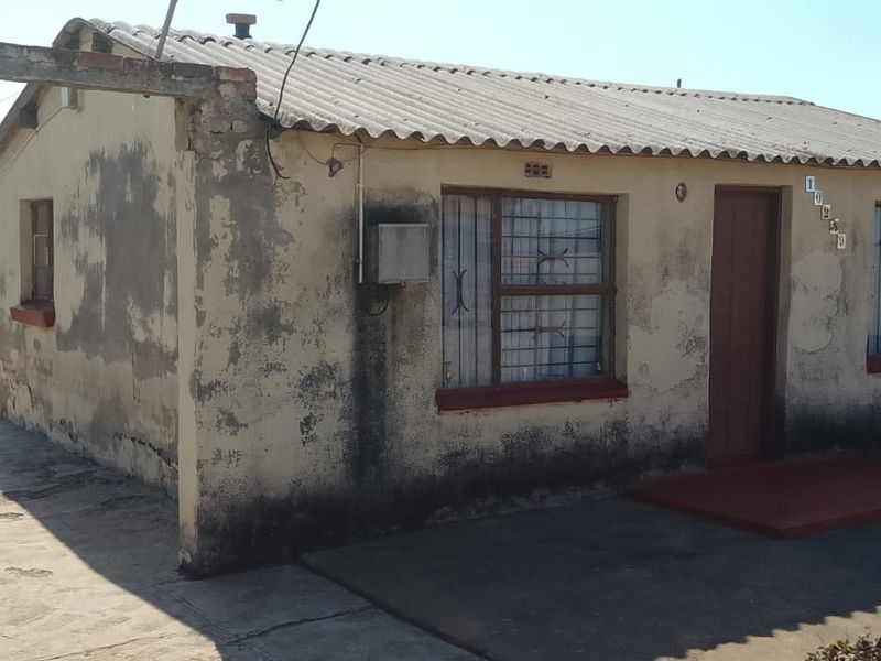 Front elevation of a detached house featuring a corrugated roof, security bars on windows, and a concrete driveway requiring maintenance.