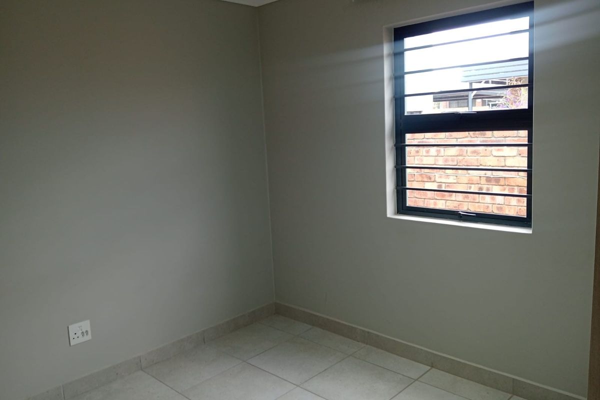 A clean, empty bedroom featuring neutral wall paint, tiled flooring, and a window fitted with security bars.