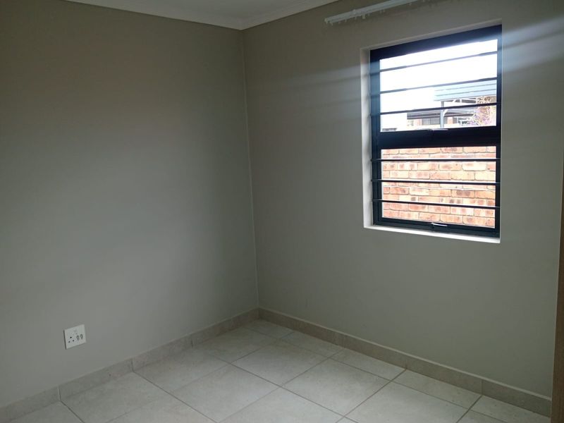 A clean, empty bedroom featuring neutral wall paint, tiled flooring, and a window fitted with security bars.
