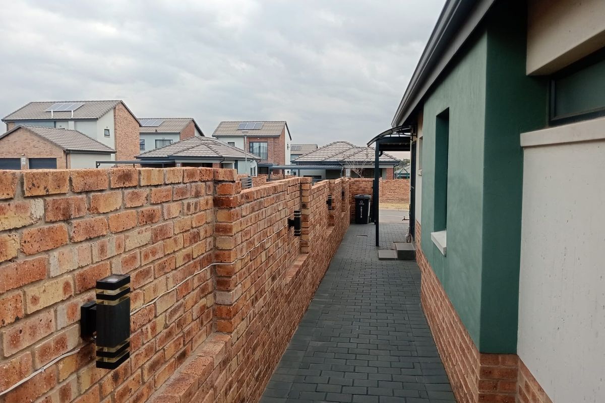 A side walkway featuring a paved path, face brick boundary wall with integrated lighting, and a painted exterior wall.