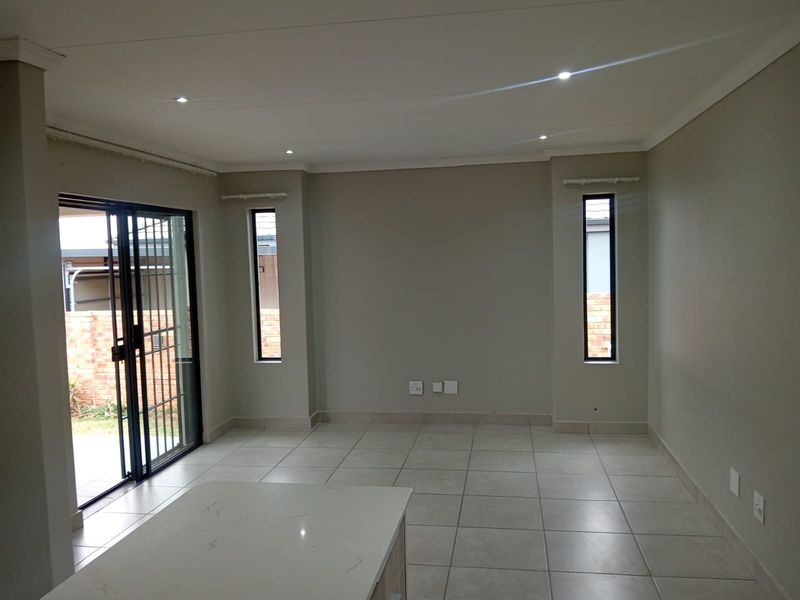 Spacious open-plan living area featuring neutral tiled flooring, recessed downlighting, and a sliding glass door providing access to the exterior.
