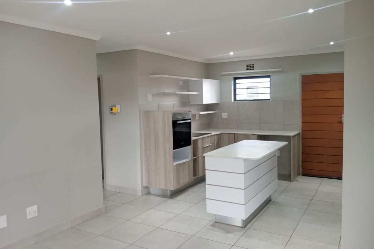 Modern kitchen featuring a central island, built-in oven, light wood cabinetry, stone countertops, and neutral tiled flooring in an open-plan layout.