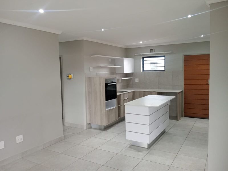 Modern kitchen featuring a central island, built-in oven, light wood cabinetry, stone countertops, and neutral tiled flooring in an open-plan layout.