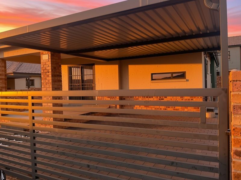 Front exterior view of the property featuring a modern metal carport, paved driveway, and secure metal gate entrance at sunset.