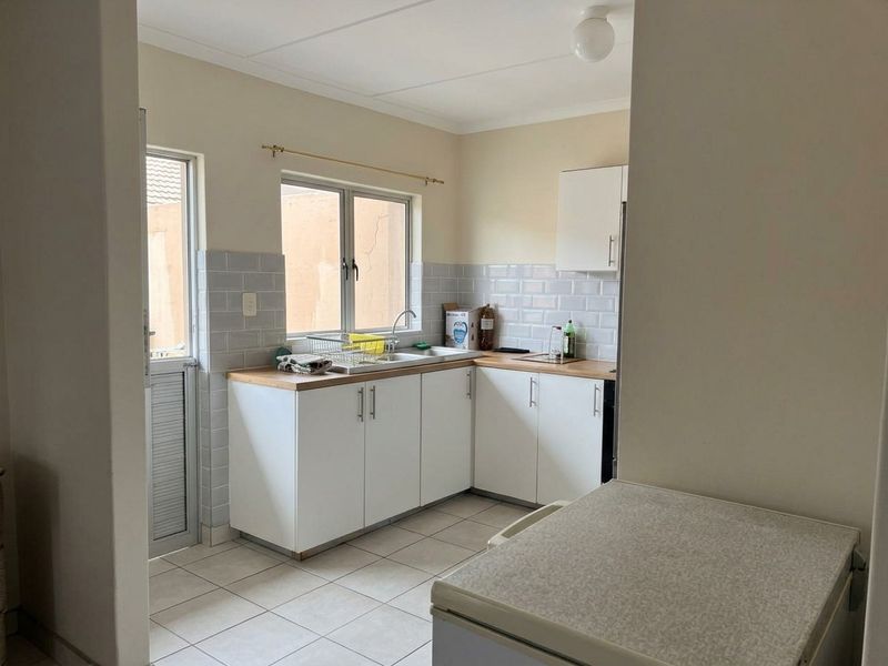 Functional kitchen featuring white cabinetry, subway tile backsplash, light-toned laminate countertops, and tiled flooring with direct access to an exterior door.