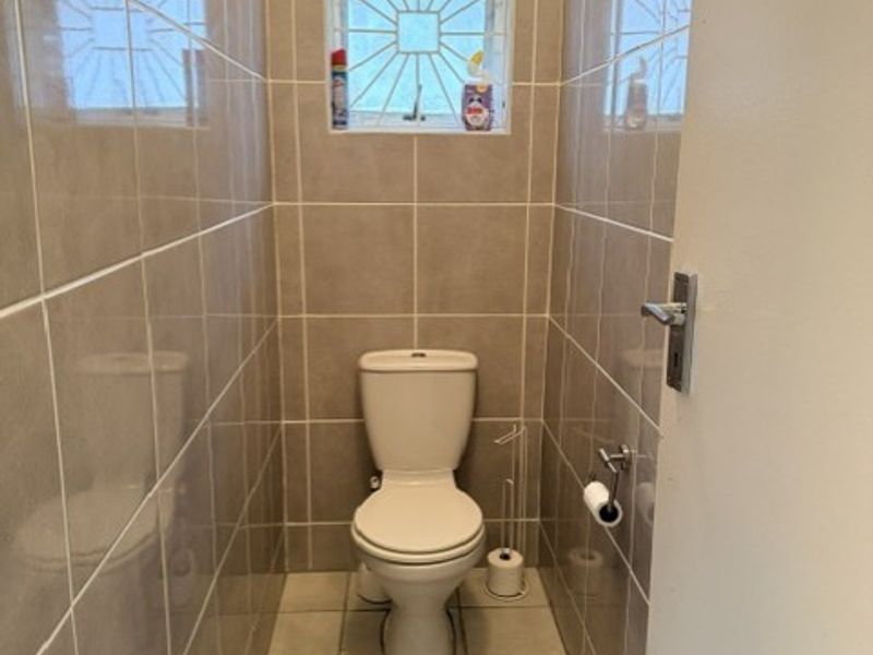 A compact, fully tiled bathroom featuring a standard toilet and a small window with security bars.