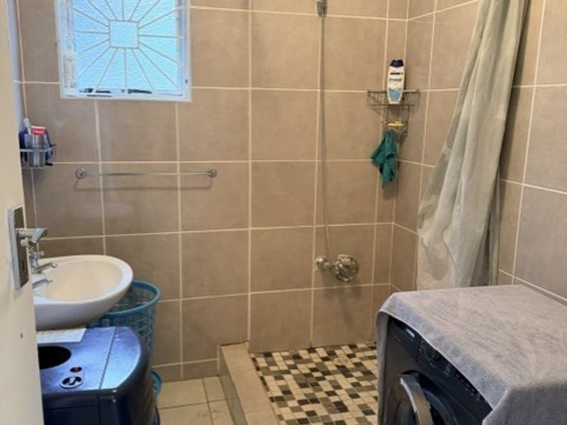 A functional bathroom featuring a tiled shower enclosure, wall-mounted washbasin, and tiled finishes throughout, providing a practical space for daily use.