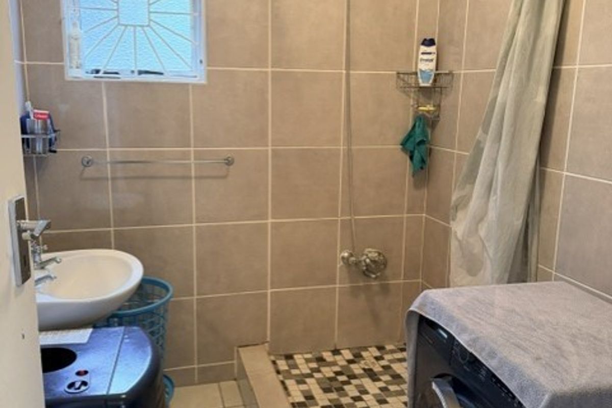 A functional bathroom featuring a tiled shower enclosure, wall-mounted washbasin, and tiled finishes throughout, providing a practical space for daily use.