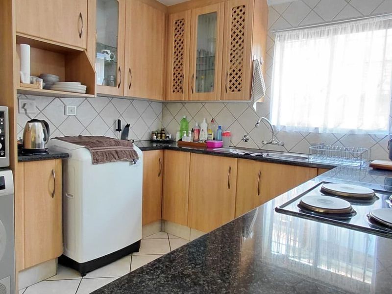 Functional kitchen featuring laminate cabinetry, granite countertops, an electric hob, and a tiled backsplash, providing a practical workspace with integrated appliance housing.