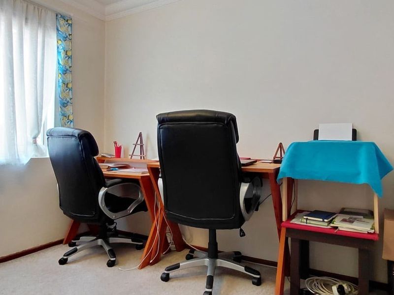 A functional home office space featuring carpeted flooring and a window with curtain treatments, suitable for a dedicated workspace or study area.