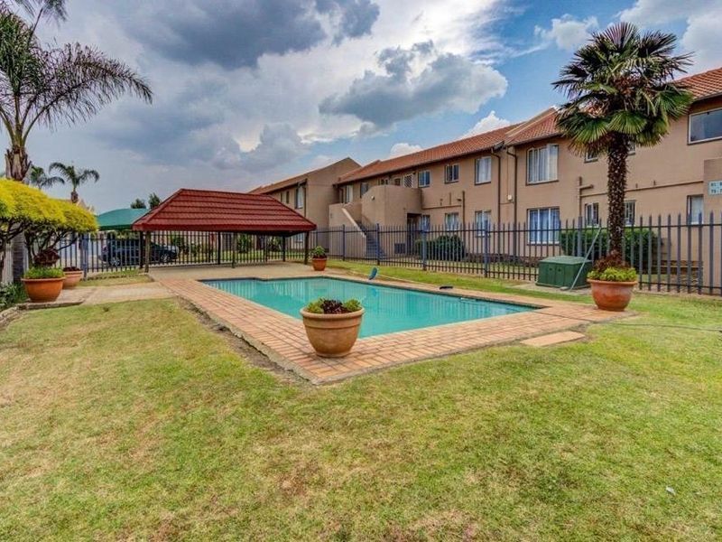 Communal outdoor pool area featuring a swimming pool, covered gazebo, and surrounding lawn within a fenced apartment complex.