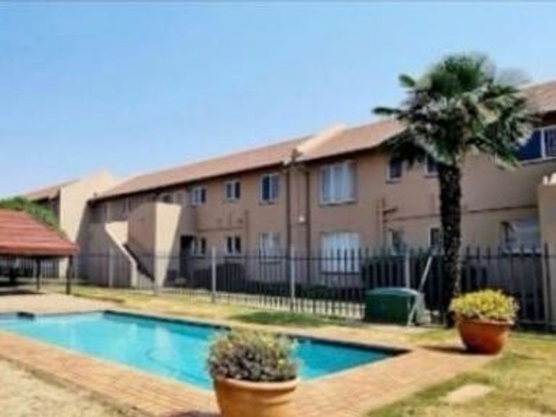 Communal pool area featuring a swimming pool, paved surround, and a covered gazebo within a fenced apartment complex.