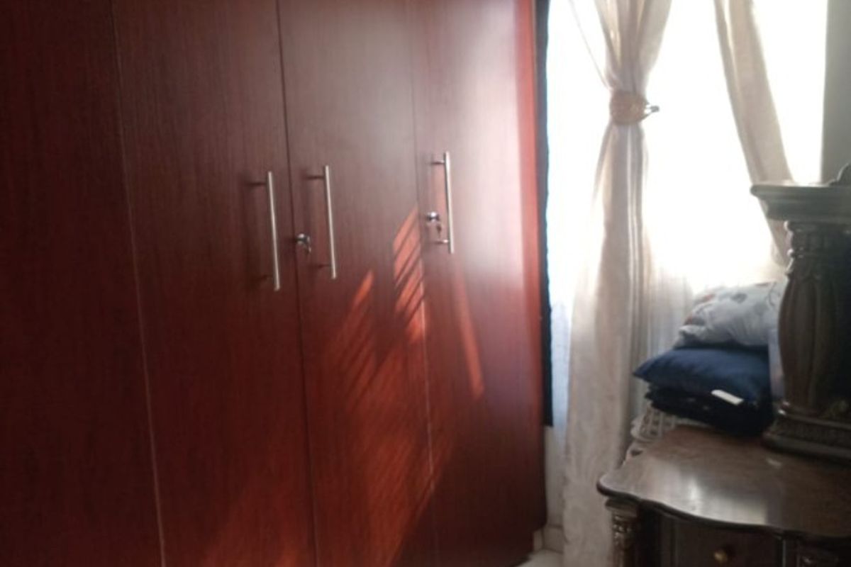 Bedroom featuring a large built-in wooden wardrobe, polished floor tiles, and natural light from the window.