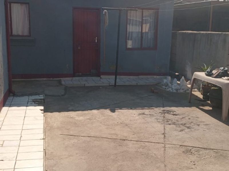 Rear exterior view of the property featuring a tiled roof, concrete paved yard, and boundary walling.