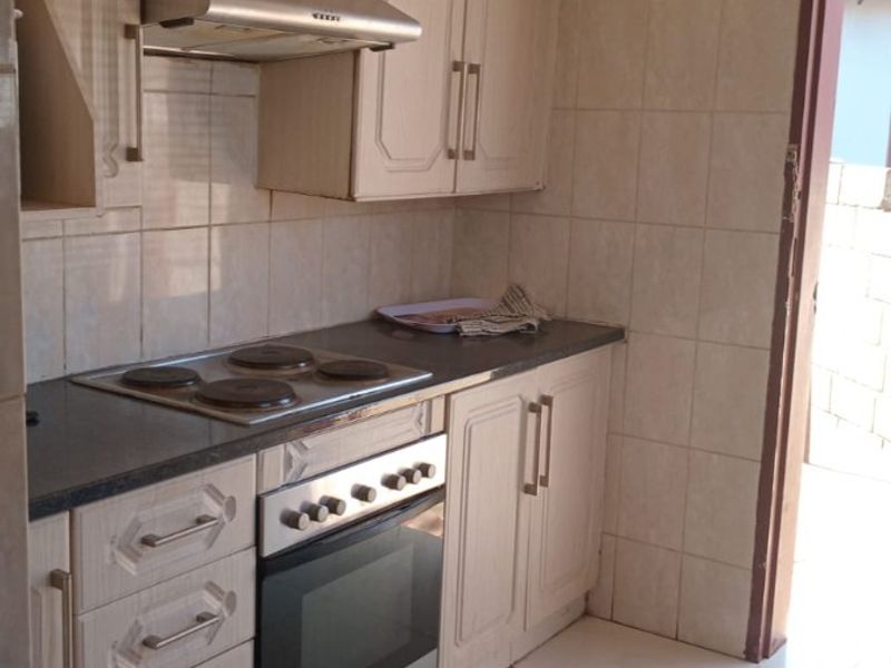 A functional kitchen featuring built-in cabinetry, an electric hob, an oven with an extractor fan, and tiled finishes throughout.