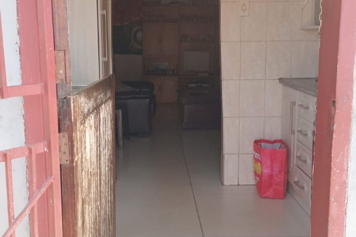 A view through a doorway into a kitchen area featuring tiled walls, flooring, and built-in cabinetry, leading to an adjacent living space.
