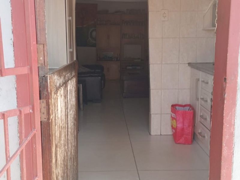 A view through a doorway into a kitchen area featuring tiled walls, flooring, and built-in cabinetry, leading to an adjacent living space.