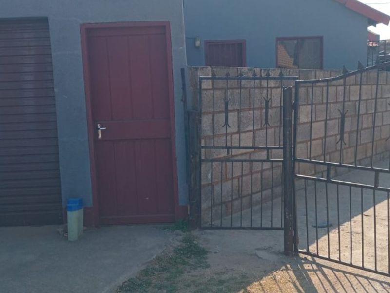 Front exterior view of the property featuring a metal garage door, security gate, and concrete driveway with a brick boundary wall.