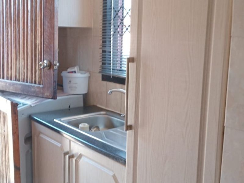 A functional scullery area featuring built-in cabinetry, a stainless steel sink, and a laminate countertop, showing signs of wear and dated finishes.
