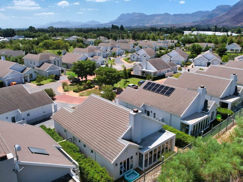 Aerial view of a residential estate featuring multiple homes with tiled roofs, solar panels, and well-maintained landscaped surroundings with mountain views.