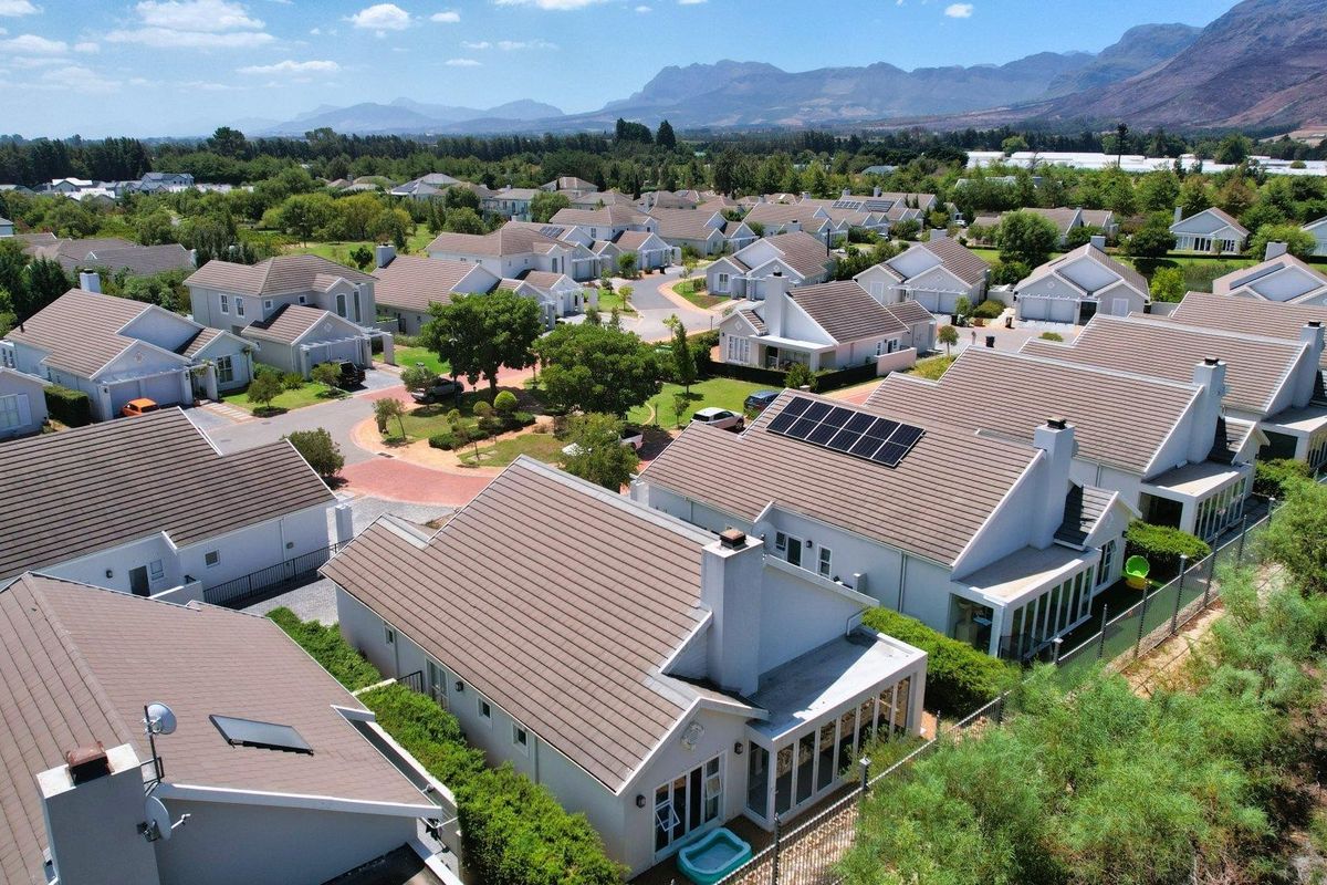 Aerial view of a residential estate featuring multiple homes with tiled roofs, solar panels, and well-maintained landscaped surroundings with mountain views.