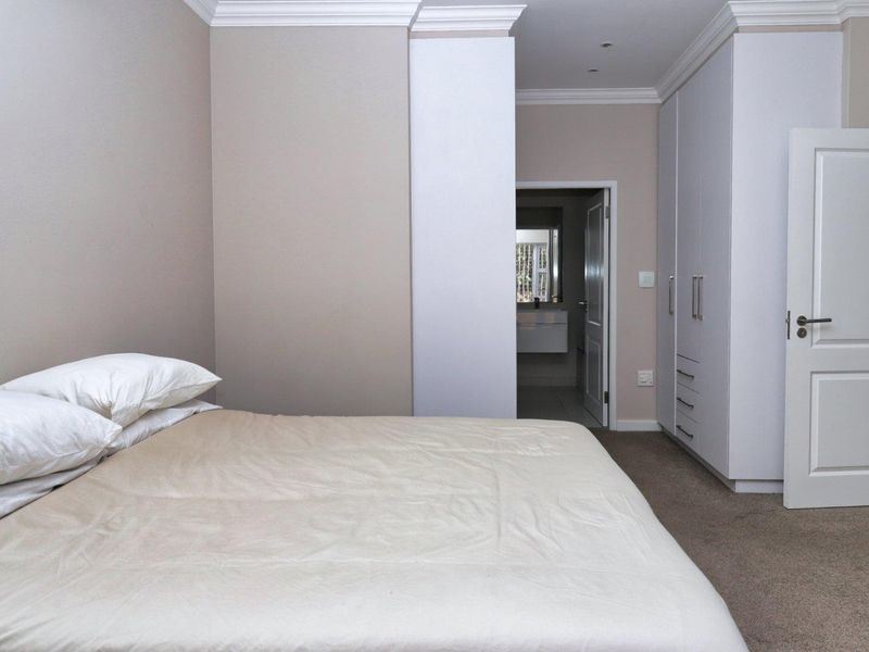 A well-maintained bedroom featuring neutral wall tones, built-in cupboards, crown molding, and carpeted flooring, with an adjoining en-suite bathroom.
