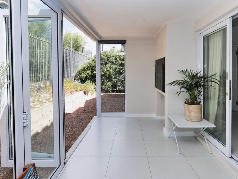 A bright, covered patio area featuring large bi-fold doors, tiled flooring, and a built-in fireplace, offering seamless indoor-outdoor flow to the garden.
