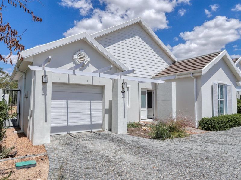 Front elevation of a well-maintained house featuring a single garage, pergola, and a paved cobblestone driveway.