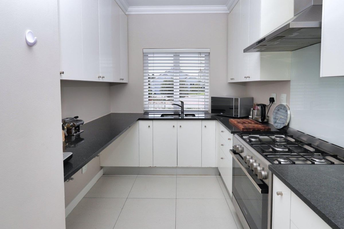 A modern galley-style kitchen featuring white cabinetry, dark stone countertops, a gas cooktop with extractor fan, and tiled flooring.
