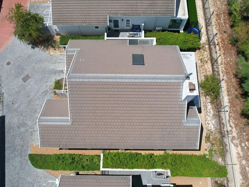 Aerial view of the property showcasing the tiled roof, chimney, skylight, and surrounding paved driveway and landscaped garden areas.