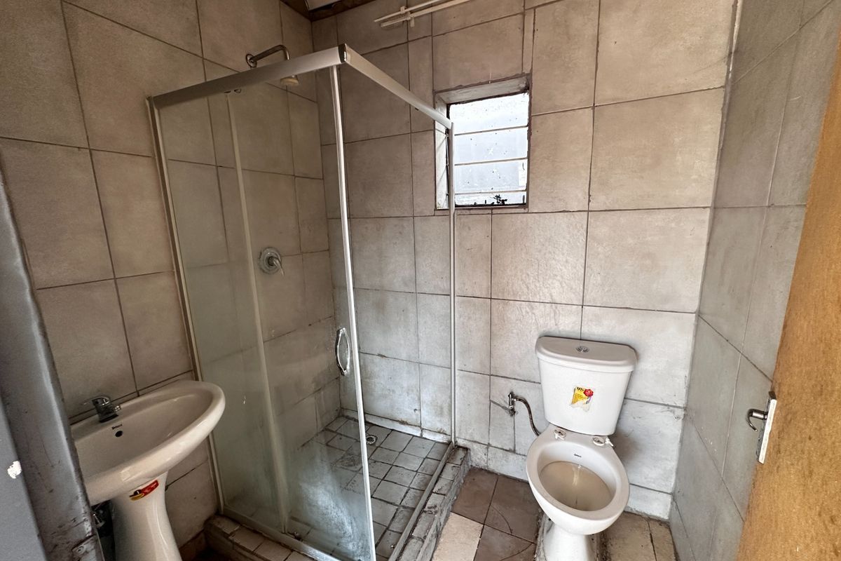 A compact bathroom featuring a pedestal basin, shower enclosure, and toilet, with tiled finishes requiring maintenance and refurbishment.