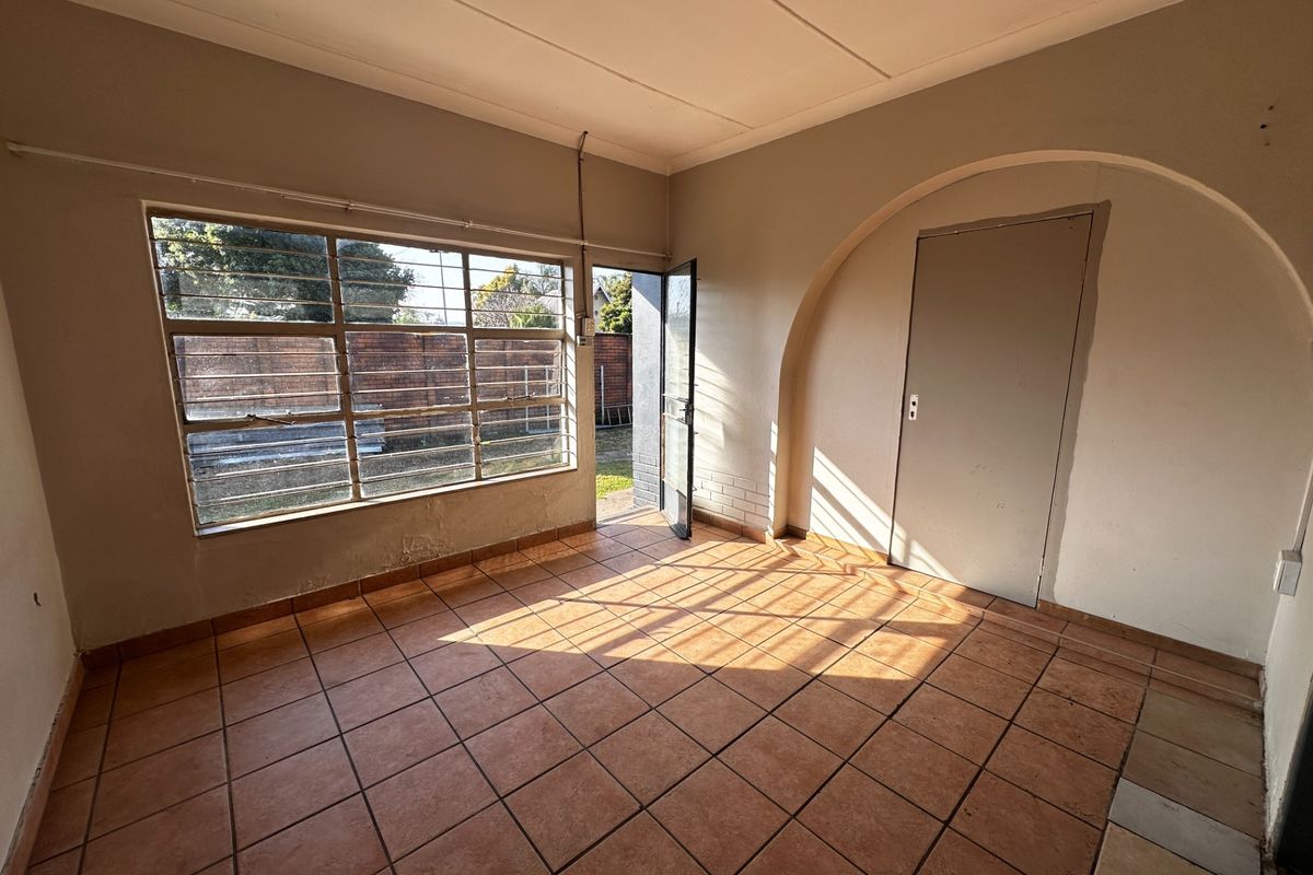 An empty living area featuring tiled flooring, a large steel-framed window, and a distinctive arched doorway leading to an adjacent room.