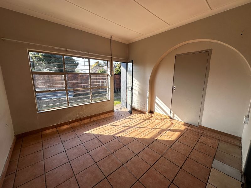 An empty living area featuring tiled flooring, a large steel-framed window, and a distinctive arched doorway leading to an adjacent room.
