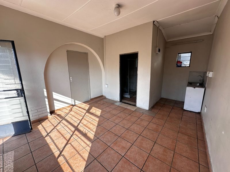 An empty open-plan living area featuring tiled flooring, an arched doorway, and a basic kitchenette sink unit.