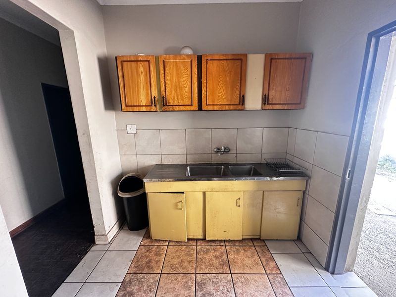 A functional scullery area featuring a stainless steel double sink, tiled splashback, and dated wall and floor-mounted cabinetry.