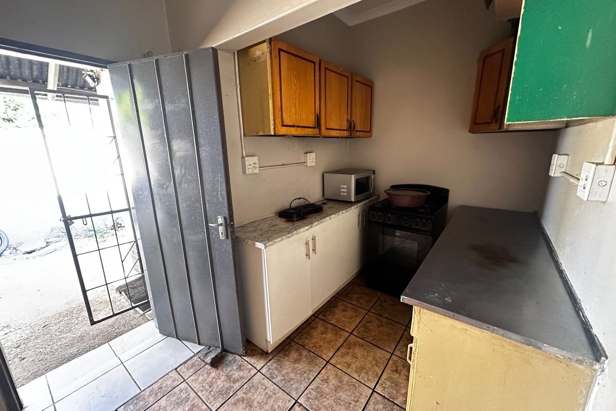 A compact kitchen featuring built-in cabinetry, laminate countertops, and a freestanding stove, with direct access to an outdoor area via a security gate.