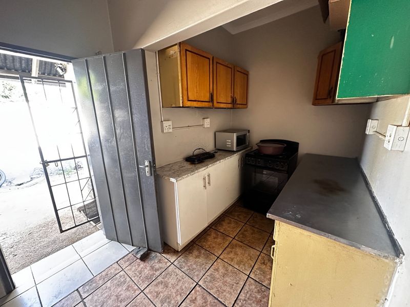 A compact kitchen featuring built-in cabinetry, laminate countertops, and a freestanding stove, with direct access to an outdoor area via a security gate.