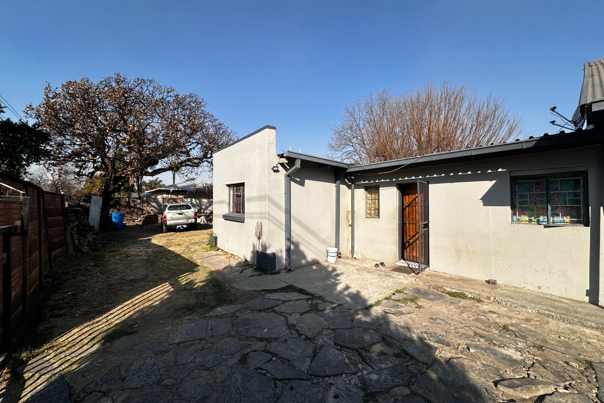 Rear exterior view of the property featuring a stone paved patio area, security gates, and window bars, set against a large garden space.